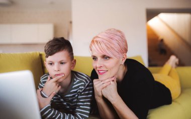 Evde kanepede dizüstü kullanarak küçük oğlu olan genç bir kadın.