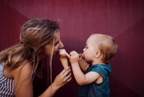 A kis tipegő lány nyáron szabadban, eszik fagylaltot fiatal anya. — Stock Fotó