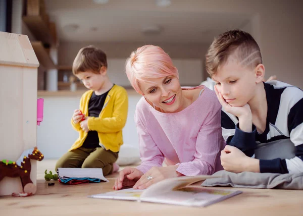 Una giovane donna con due bambini che legge un libro e gioca sul pavimento . — Foto Stock