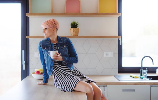 A young attractive woman sitting on a counter in a kitchen at home. — Stock Photo, Image