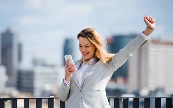 Una joven mujer de negocios con teléfono inteligente de pie en una terraza, expresando emoción . —  Fotos de Stock