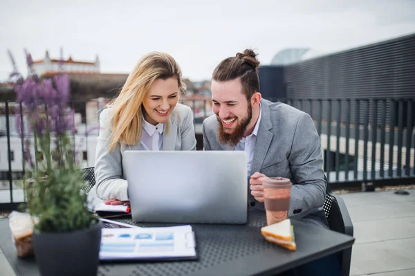 Zwei junge Geschäftsleute mit Laptop sitzen auf einer Terrasse vor dem Büro und arbeiten. — Stockfoto