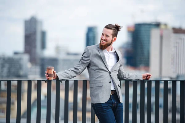 Un jeune homme d'affaires avec café debout sur une terrasse, au repos . — Photo