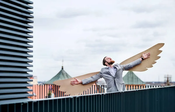 Un jeune homme d'affaires avec des ailes debout sur une terrasse, concept de métaphore volante . — Photo