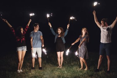 A group of friends with sparklers standing outdoors at dusk. clipart