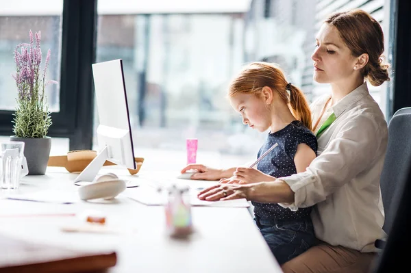 Eine Geschäftsfrau mit kleiner Tochter sitzt in einem Büro und arbeitet. — Stockfoto