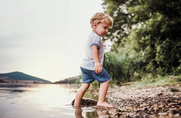 En våt, små barn pojke står utomhus i en flod på sommaren, spela. — Stockfoto