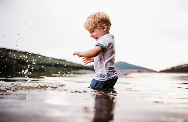 Un niño mojado y pequeño parado al aire libre en un río en verano, jugando . — Foto de Stock