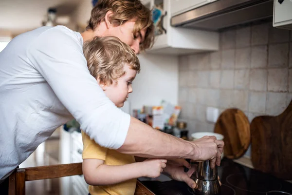 Un giovane padre con un figlio piccolo in cucina a casa . — Foto Stock