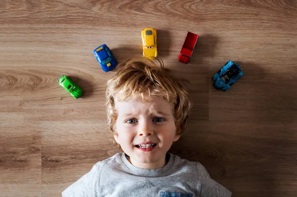 Una vista superior de un niño pequeño con coches de juguete tirados en el suelo en casa . — Foto de Stock