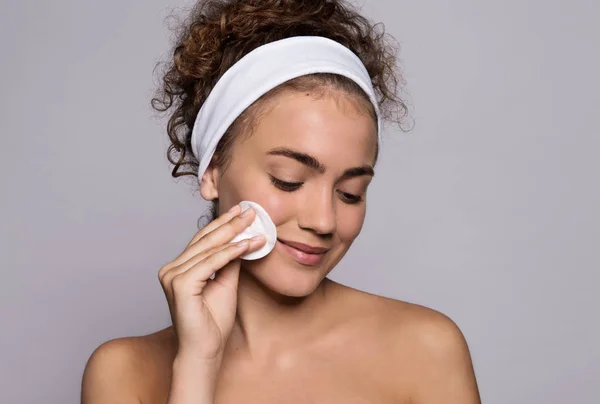 Un retrato de una joven limpiando la cara en un estudio, belleza y cuidado de la piel . — Foto de Stock