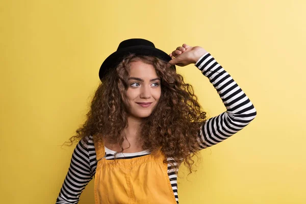 Retrato de uma jovem mulher com chapéu preto em um estúdio em um fundo amarelo . — Fotografia de Stock