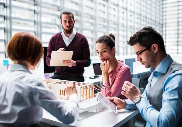 Group of young architects with model of a house working in office, talking. — Stock Photo, Image