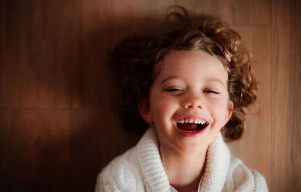 Um retrato de menina pequena com suéter de malha branca deitada no chão, uma vista superior . — Fotografia de Stock