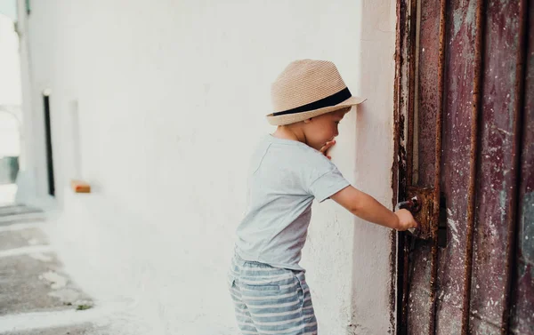 Um menino pequeno com chapéu em pé perto de uma casa na cidade em férias de verão . — Fotografia de Stock