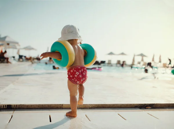 Rückansicht eines kleinen Kindes mit Armbinden, das im Sommerurlaub am Strand spaziert. — Stockfoto