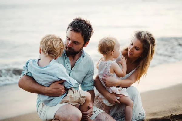 Una familia con dos niños pequeños sentados en la playa de arena en las vacaciones de verano . — Foto de Stock