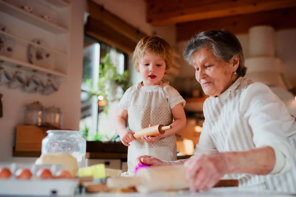 自宅でケーキを作る小さな幼児男の子とシニアの祖母. — ストック写真