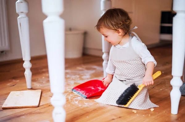 A small toddler girl with brush and dustpan sweeping floor in the kitchen at home. — Stock Photo, Image