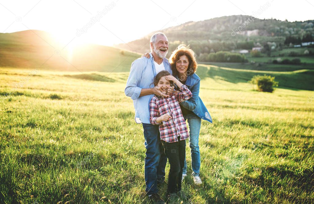 Senior couple with granddaughter standing outside in spring nature at sunset.