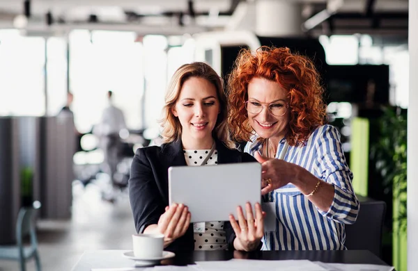 Zwei Geschäftsfrauen mit Tablet sitzen im Büro und unterhalten sich. — Stockfoto