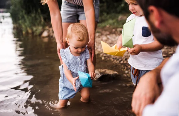 Una sección media de la familia con dos niños pequeños al aire libre junto al río en verano . — Foto de Stock