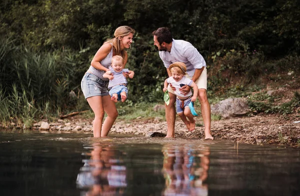 En ung familj med två småbarn barn utomhus vid floden i sommar. — Stockfoto