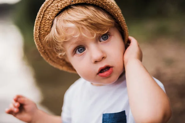 Um menino pequeno de pé ao ar livre junto a um rio no verão . — Fotografia de Stock