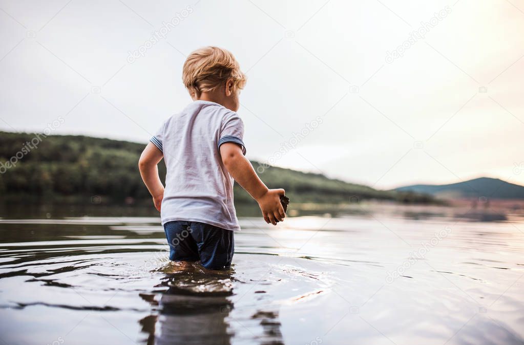 A wet, small toddler boy walking outdoors in a river in summer, playing.