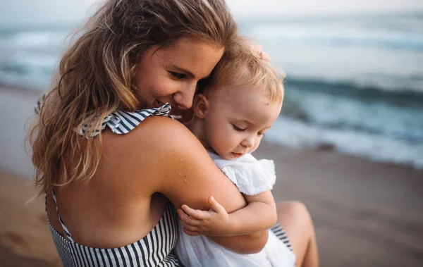 Close-up of young mother with a toddler girl on beach on summer holiday. — Stock Photo, Image