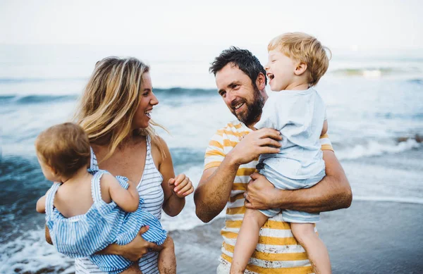 Una familia joven con dos niños pequeños de pie en la playa en las vacaciones de verano . —  Fotos de Stock