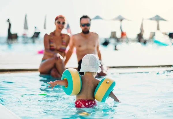 Ett litet barn med armband och föräldrar i SIM bassäng på sommarlovet. — Stockfoto