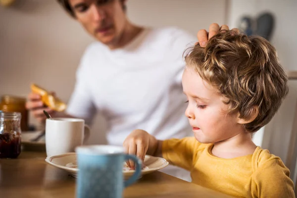 Jovem pai com um filho menor tomando café da manhã em casa . — Fotografia de Stock