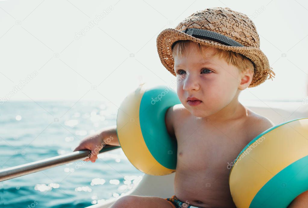 A small boy with armbands sitting on boat on summer holiday.