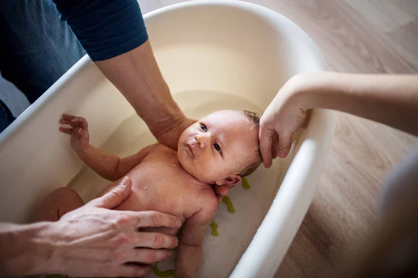 Parents méconnaissables donnant un bain à un nouveau-né à la maison . — Photo