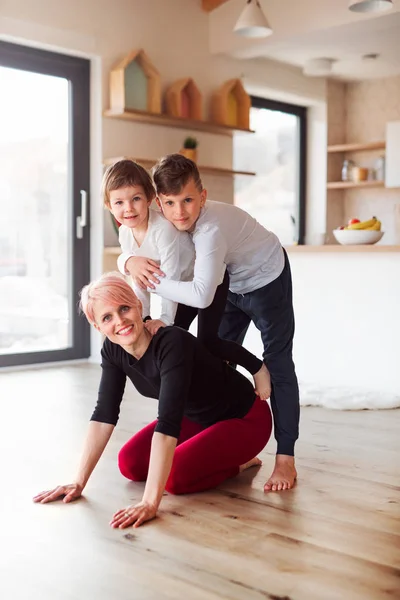 Uma jovem mulher com dois filhos dentro de casa, olhando para a câmera . — Fotografia de Stock