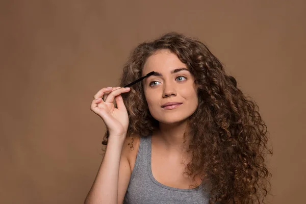 Portrait of a young woman applying make-up in a studio against brown background. — Stock Photo, Image