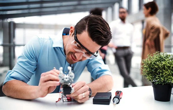 Ein junger Geschäftsmann oder Wissenschaftler mit Roboterhand, der im Büro steht und arbeitet. — Stockfoto