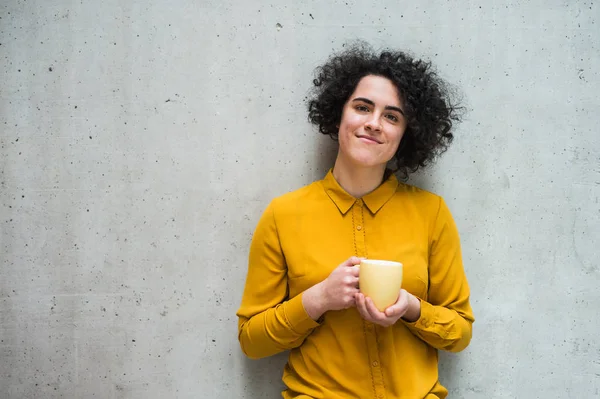 Um retrato da jovem empresária em pé no escritório, segurando uma xícara de café . — Fotografia de Stock