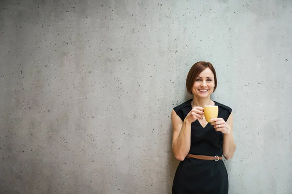 Porträt einer jungen Geschäftsfrau, die mit einer Tasse Kaffee im Büro steht. — Stockfoto