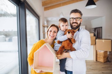 Yeni evinde hareketli bir yürümeye başlayan çocuk kızla genç aile portresi.