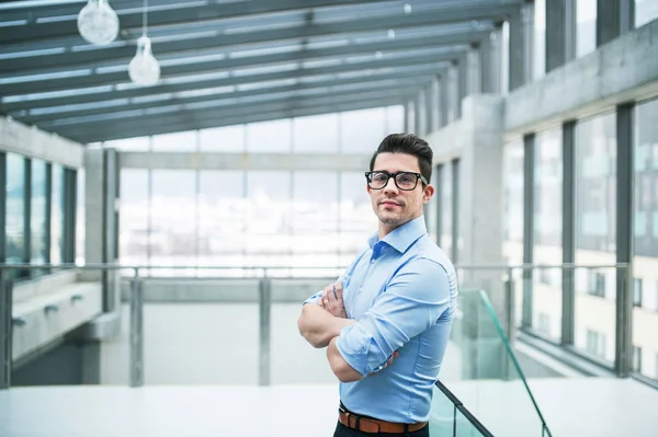 Un retrato de un joven empresario de pie en una oficina, con los brazos cruzados . —  Fotos de Stock