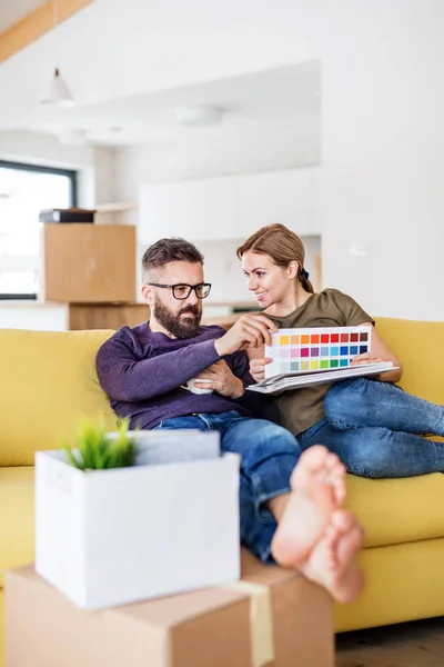 Ein junges Paar mit Farbmustern sitzt auf dem Sofa und bezieht ein neues Zuhause. — Stockfoto