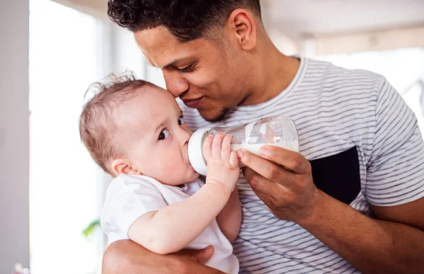 Un ritratto della bottiglia del padre che alimenta un piccolo figlio del bambino all'interno di casa . — Foto Stock