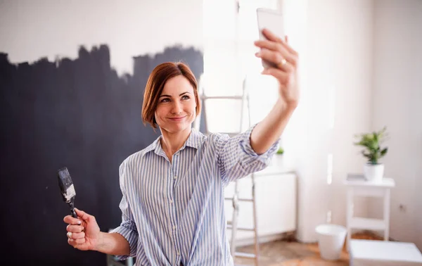 Młoda kobieta malowanie ścian czarny, biorąc selfie. Uruchomienie małych firm. — Zdjęcie stockowe