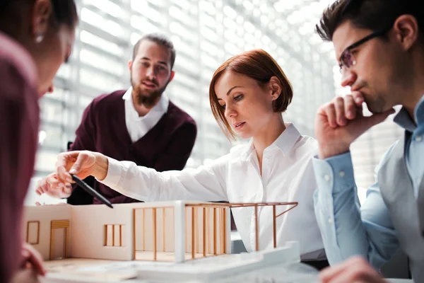 Groep van jonge architecten met model van een huis die werken met office, praten. — Stockfoto