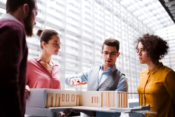 Group of young architects with model of a house standing in office, talking. — Stock Photo, Image