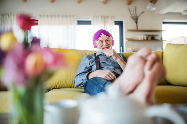 A senior man with headphones and eye mask sitting on sofa indoors at home. — Stock Photo, Image