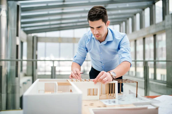 Ung affärsman eller arkitekt med modell av ett hus stående på kontoret, arbetar. — Stockfoto