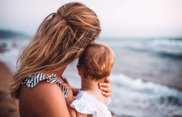 Vista posteriore della giovane madre con una bambina sulla spiaggia in vacanza estiva . — Foto Stock